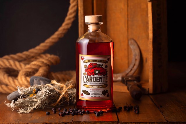 Bottiglia di Sanguamaro Amaro IPA de L'Ardente Micro Distilleria Artigiana con radici e cortecce in primo piano