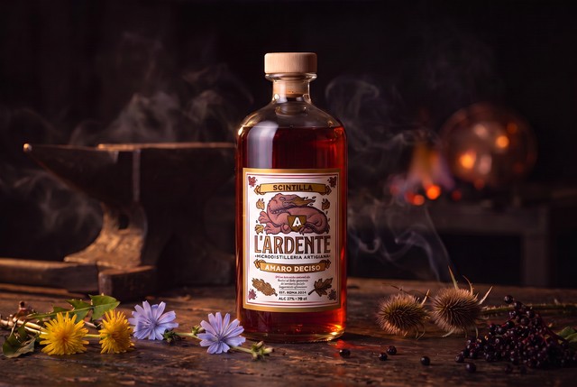 Bottiglia di Scintilla Amaro Deciso de L'Ardente Micro Distilleria Artigiana su banco da fabbro con incudine, brace, tarassaco, cicoria e bacche di sambuco